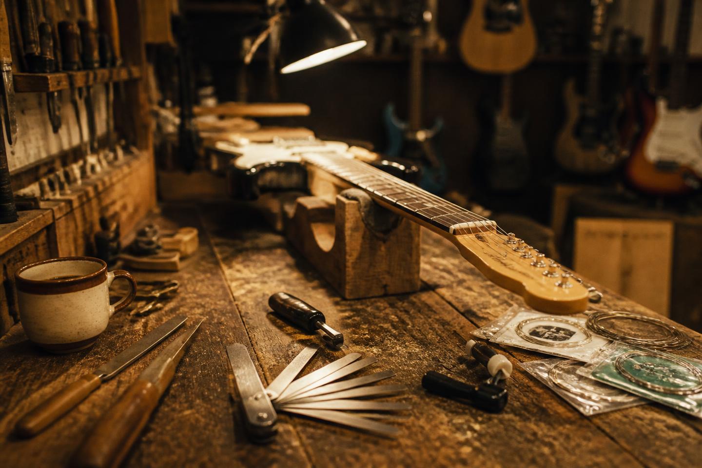 A guitar technician's workbench with a guitar neck in a cradle, feeler gauges, files and fresh strings